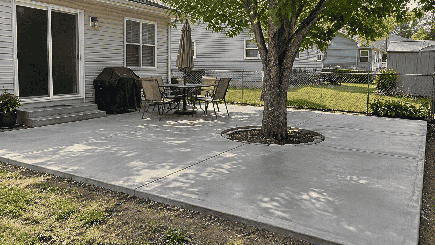 Backyard concrete patio with tree cutout, outdoor seating, and realistic landscaping showing a simple DIY patio upgrade.