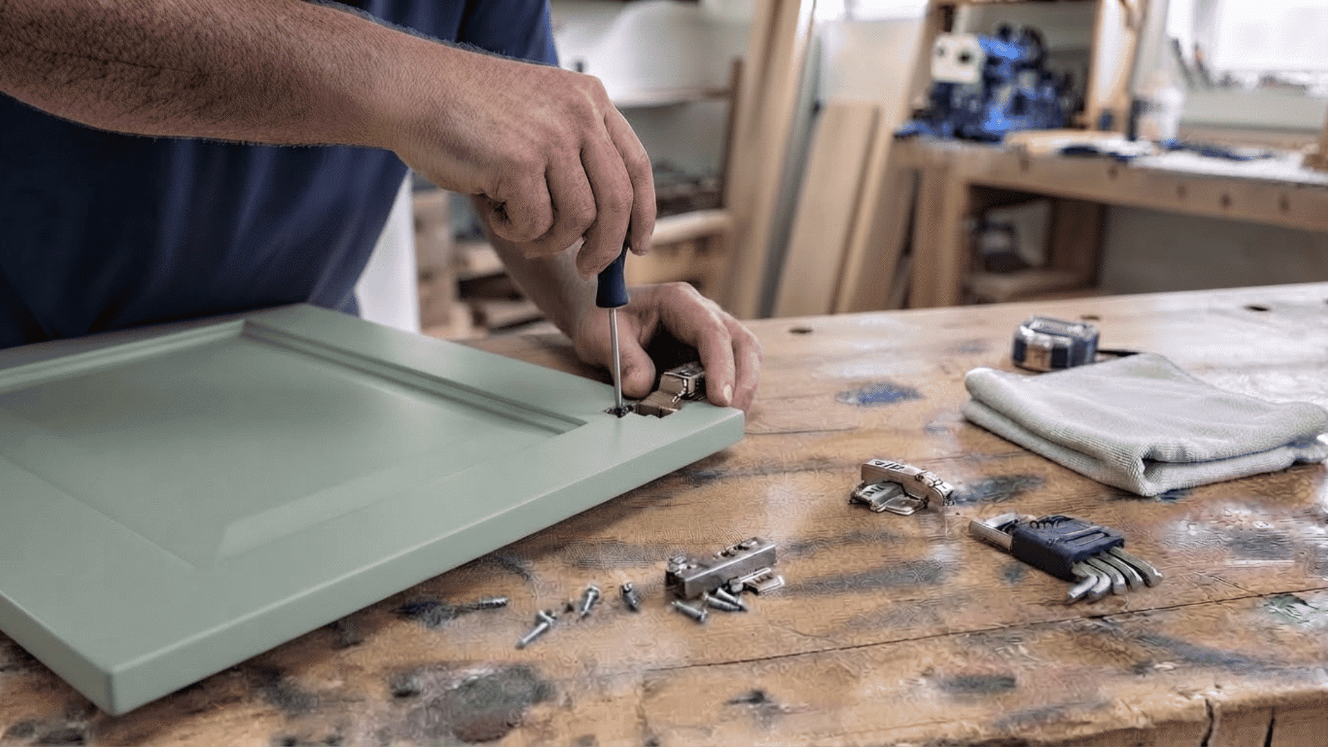 Hands installing cabinet hinges and adjusting a door on a cabinet frame with tools nearby
